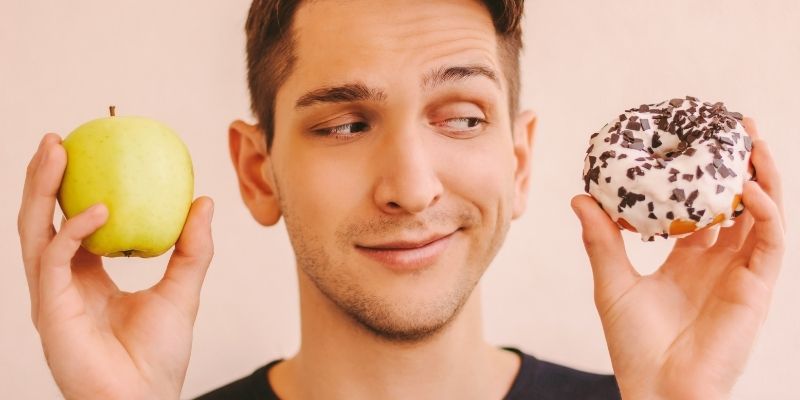 Osoba drži u rukama kolač i izgleda zbunjeno ili emotivno, simbol borbe sa dijetama.