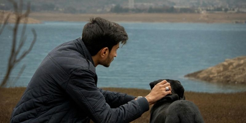 Čovek sedi pored crnog psa u mirnom okruženju